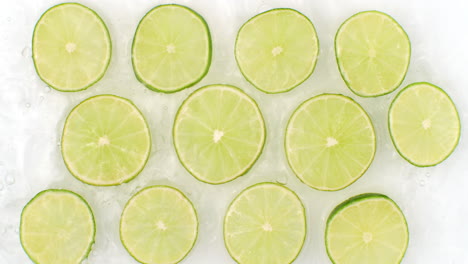 On-a-white-background-sliced-pieces-of-lime-are-sprinkled-with-water.-Juicy-fresh-lime-in-slow-motion.-Lots-of-lime-slices.